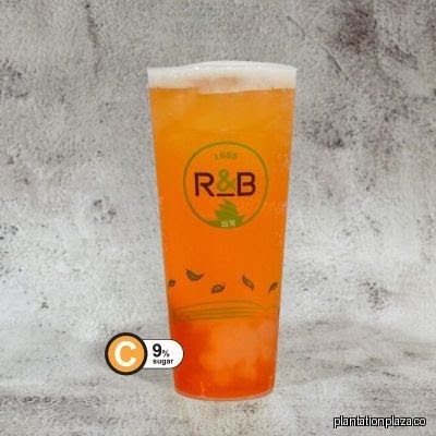 An orange drink in a clear cup with R&B logo and 9% sugar label.